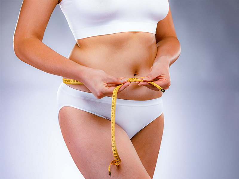A imagem mostra uma mulher medindo a circunferência da sua barriga antes da abdominoplastia