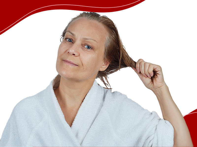 Mulher de roupão branco e segurando o cabelo molhado para trás, para mostrar o que é alopecia